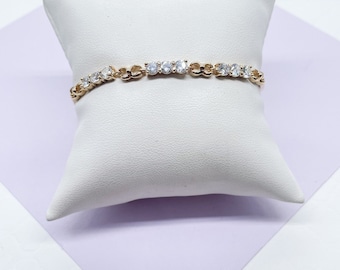 Puede incluir: Un brazalete de cadena dorada con piedras de circonita cúbica transparentes. El brazalete está sobre una almohada blanca.