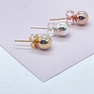 May include: Three pairs of stud earrings with a round ball design. The earrings are made of gold, silver, and rose gold.