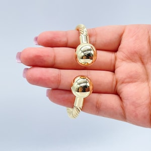 May include: A gold bangle bracelet with a twisted rope design and two round ball ends.