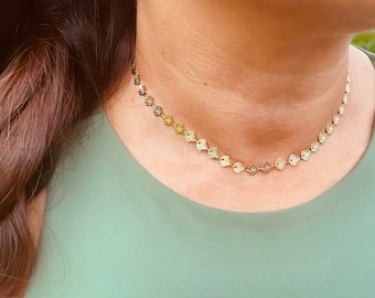 May include: A gold necklace with a delicate chain and small, textured heart-shaped charms. The necklace is worn by a person with long brown hair.