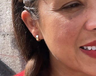 May include: A close-up of a person's ear with a small gold hoop earring. The earring is simple and elegant.