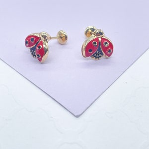 May include: A pair of gold ladybug earrings with red and black enamel. The earrings are on a white surface.