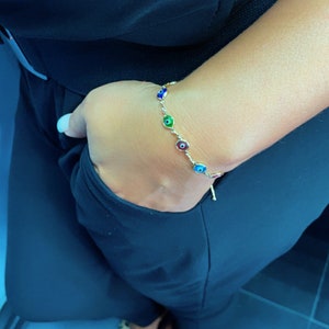 May include: A gold bracelet with a chain and multiple colorful evil eye charms. The bracelet is on a person's wrist.