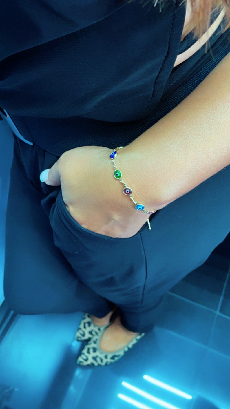 May include: A gold bracelet with a chain and multiple colorful evil eye charms. The bracelet is on a person's wrist.