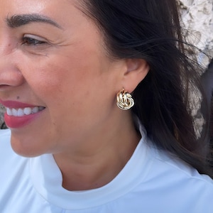 May include: Gold knot-shaped earrings. The earrings are a simple design with a twisted knot shape.
