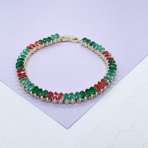 Op de afbeelding: Een goudkleurige armband met een herhalend patroon van rechthoekige rode, groene en turquoise edelstenen. De armband wordt met een sluiting vastgezet. De edelstenen zijn gezet in een goudkleurig metaal.