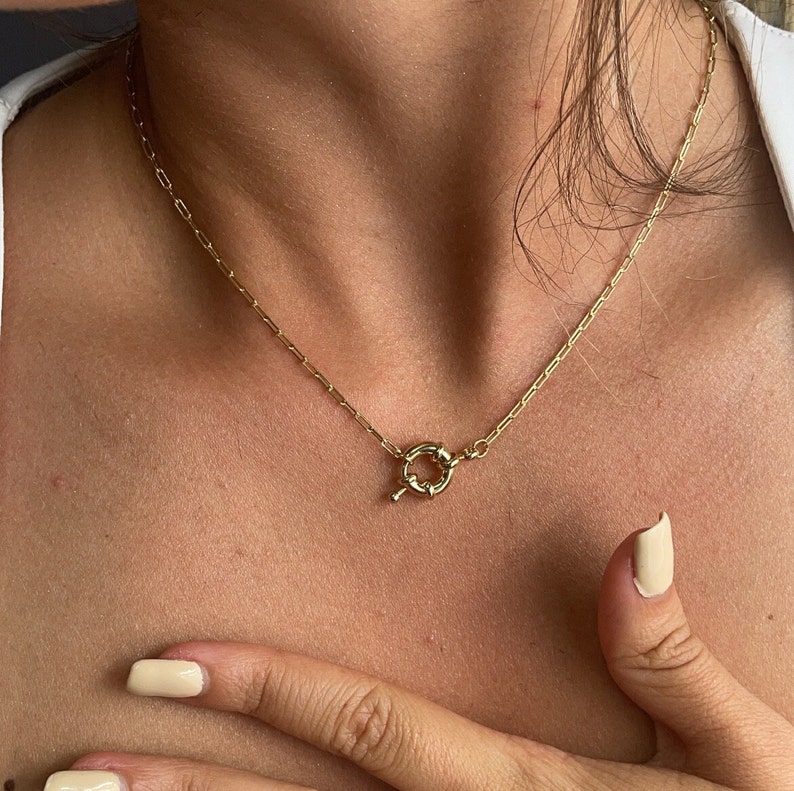 May include: A gold chain necklace with a unique, twisted, circular clasp.
