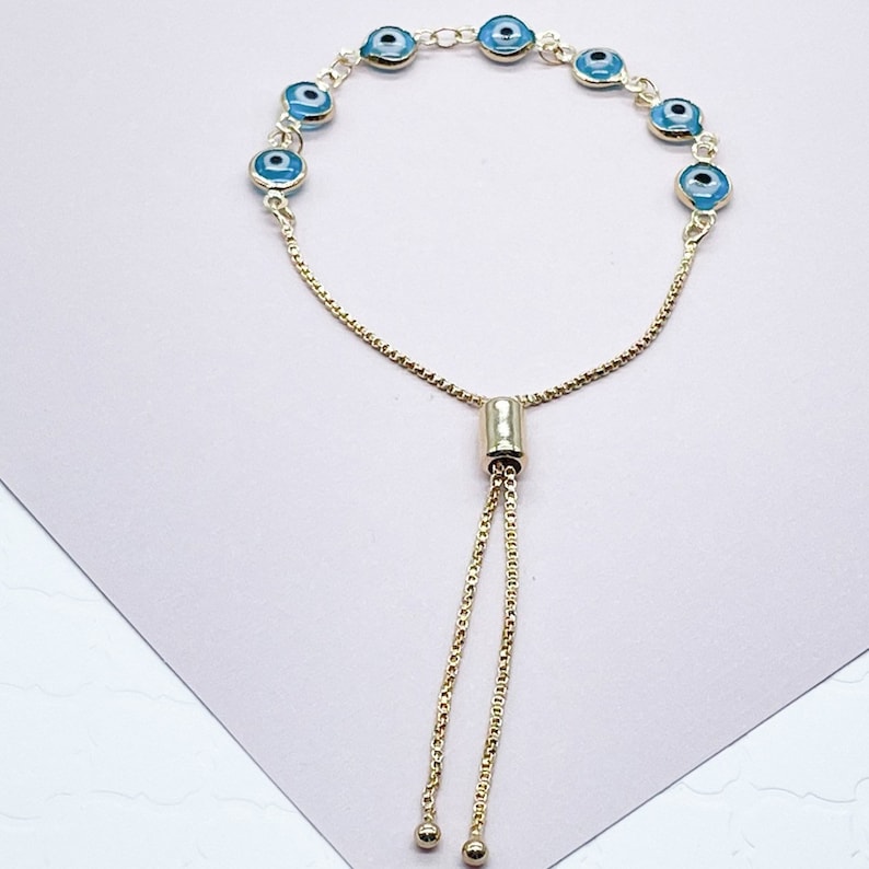 May include: A gold chain bracelet with blue evil eye charms. The bracelet has an adjustable sliding clasp.