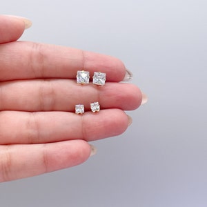 May include: Three pairs of square-shaped cubic zirconia stud earrings in gold settings. The earrings are arranged in order of size, with the largest pair at the top and the smallest pair at the bottom.