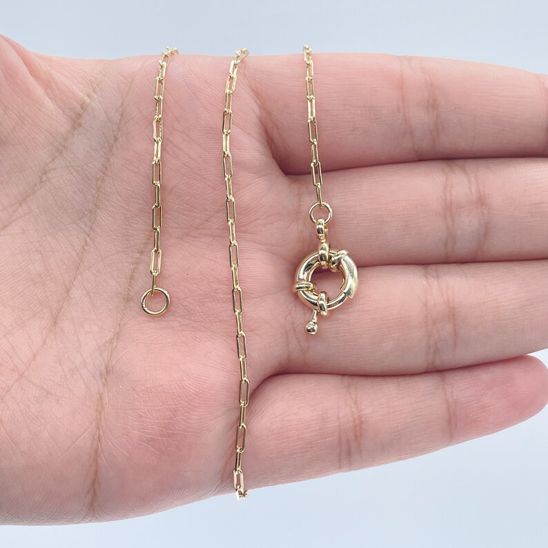 May include: A gold chain necklace with a round, twisted clasp. The chain is made of small, linked squares.