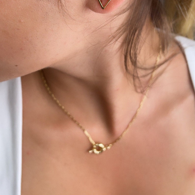 May include: A gold necklace with a knot-shaped pendant. The necklace is on a person's chest.