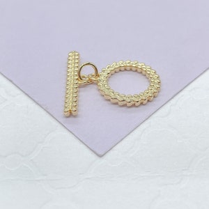 May include: Gold-toned metal toggle clasp with a round ring and a straight bar. The clasp has a textured design.