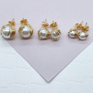 May include: Three pairs of gold pearl earrings with a delicate wire design. The earrings are arranged in order of size, with the largest pair on the left and the smallest pair on the right.