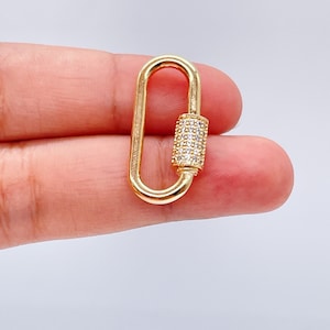 May include: Gold-toned metal clasp with a clear crystal-encrusted barrel. The clasp is oval-shaped and has a spring-loaded closure.