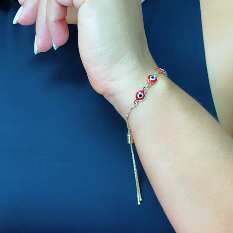 May include: A gold chain bracelet with red and blue evil eye charms. The bracelet has an adjustable sliding clasp.