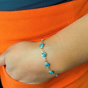 May include: A gold chain bracelet with blue evil eye charms. The bracelet is on a person's wrist.