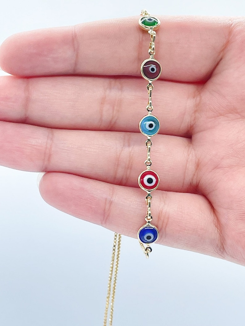 May include: A gold chain bracelet with five evil eye charms. The charms are blue, red, green, blue, and red. The evil eyes are all facing the same direction.