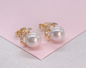 Könnte beinhalten: Ein Paar goldene Ohrringe mit einem Halbmond-Design und einer weißen Perle. Die Ohrringe sind mit kleinen, klaren Steinen besetzt.