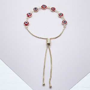 May include: A gold chain bracelet with red evil eye charms. The bracelet has an adjustable sliding clasp.