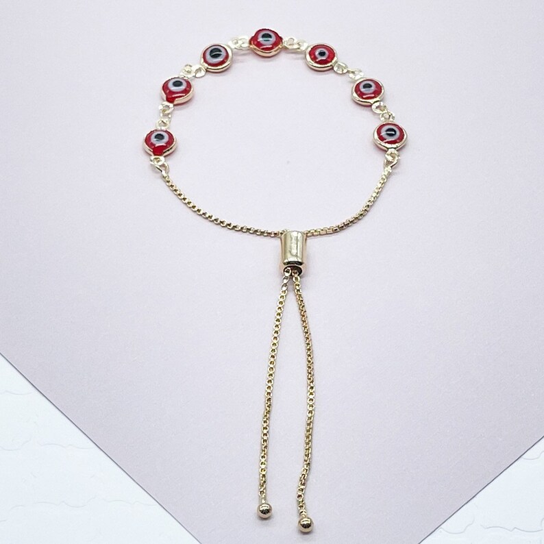 May include: A gold chain bracelet with red evil eye charms. The bracelet has an adjustable sliding clasp.