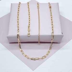 Pode incluir: Um colar de corrente de ouro com estilo de corrente de caixa. O colar est&aacute; sobre uma superf&iacute;cie rosa.