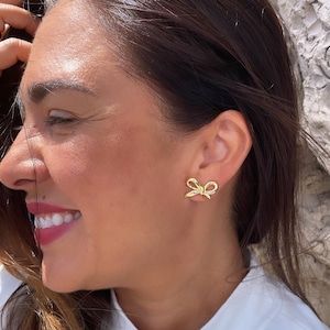 May include: A pair of gold bow-shaped earrings. The earrings are small and delicate, and they are a popular style for women.