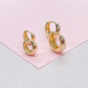 May include: Three pairs of gold hoop earrings of different sizes. The earrings are on a pink background.