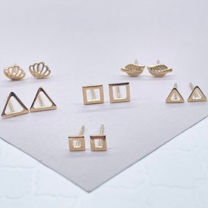 May include: A collection of gold-colored stud earrings in various geometric shapes, including triangles, squares, and open-frame designs. Also included are seashell and leaf-shaped earrings. The earrings are displayed on a light-colored surface.