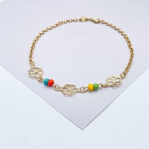 Puede incluir: Un brazalete de cadena dorada con tres pequeños abalorios de flores y cuentas de colores. Las cuentas son turquesa, naranja, amarilla y verde.