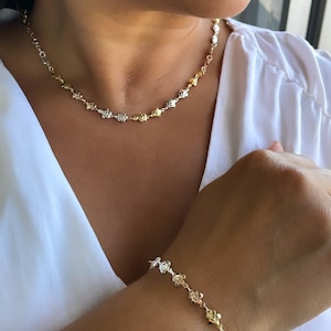 Könnte beinhalten: Eine goldene und silberne Halskette und ein Armband mit einem zarten Blumenmuster. Die Halskette und das Armband bestehen aus kleinen, miteinander verbundenen Blumen.