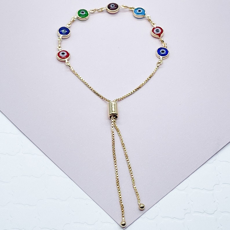 May include: A gold chain bracelet with a sliding clasp and seven colorful evil eye charms. The charms are red, blue, green, and purple.