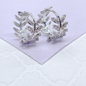 May include: A pair of silver hoop earrings with a leaf design and clear cubic zirconia stones.