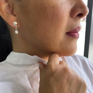 May include: A pair of gold earrings with a seashell charm and a pearl dangling from the bottom.
