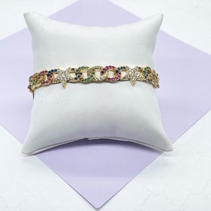 May include: Gold chain bracelet with colorful stones and star charms. The bracelet is on a white pillow.