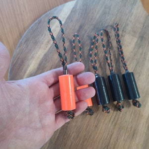 May include: Five orange and black keychains with a loop at the top. The keychains have a cylindrical shape and are made of a hard material.