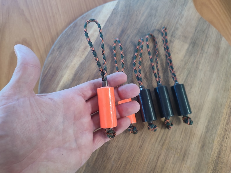 May include: Five orange and black keychains with a loop at the top. The keychains have a cylindrical shape and are made of a hard material.