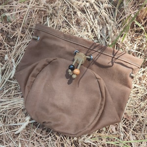 Op de afbeelding: Een bruine canvas trekkoordtas met een ronde bodem. De tas heeft een zwart en bruin koord met houten kralen.