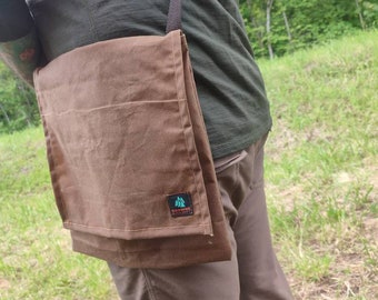 May include: A brown canvas messenger bag with a long adjustable strap, featuring a rectangular flap closure and a small black label on the lower right corner with the text BROWNS BUSHCRAFT and a graphic of three green pine trees.