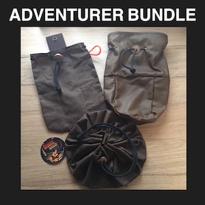May include: Three brown canvas drawstring bags with leather accents and a wooden button closure. The bags are arranged on a wooden surface.