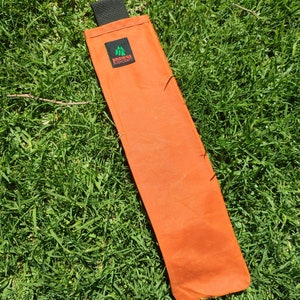 May include: An orange canvas carrying case with a black strap and a green logo that says "Browne Bushcraft".