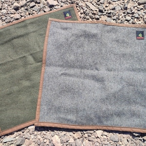 May include: Two square fabric cloths with brown stitched borders. One cloth is olive green and the other is heather gray. Each features a small black rectangular tag in the corner with the text Bigfoot Supply Co. and a green tree graphic.