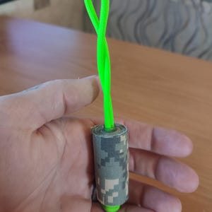 May include: A green rope with a camouflage fabric wrapped around it. The rope is tied in a loop at the top.