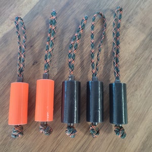 May include: Five cylindrical objects with a black and green rope attached to each. Two of the cylinders are orange and three are black.