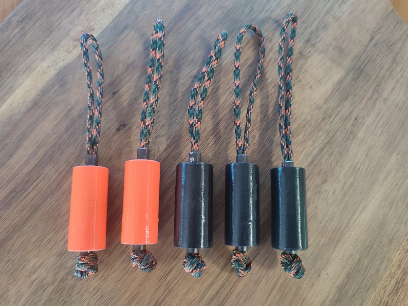 May include: Five cylindrical objects with a black and green rope attached to each. Two of the cylinders are orange and three are black.