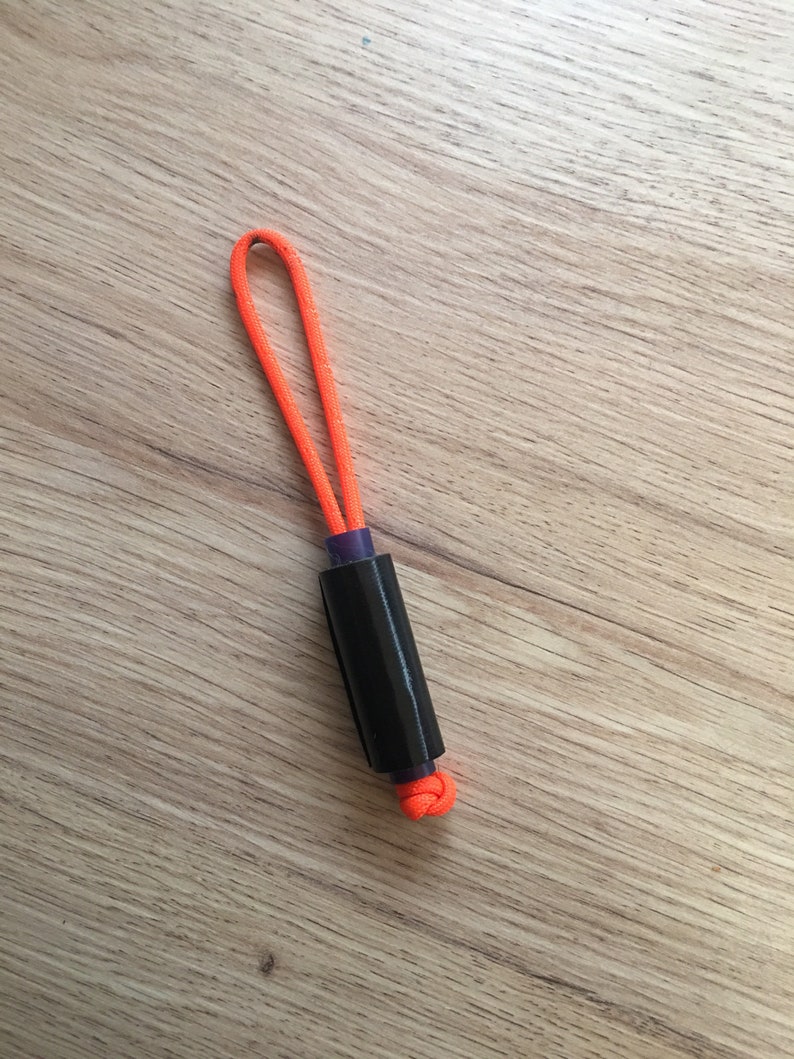 May include: A black and purple cylindrical object with an orange cord loop at the top. The cord is tied in a knot at the bottom of the object.
