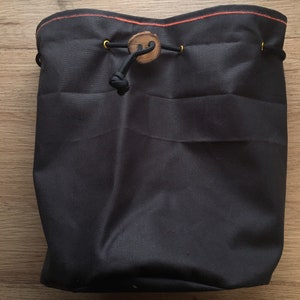 May include: A black drawstring bag with a wooden button and gold metal grommets. The bag has a red and orange stitch around the top.