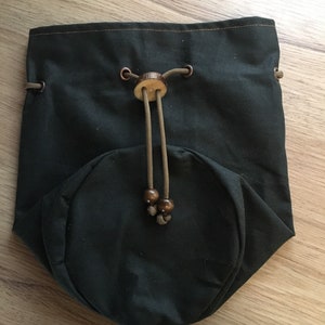 May include: A dark green drawstring bag with a wooden toggle and brown beads. The bag is made of a sturdy fabric and has a round bottom.