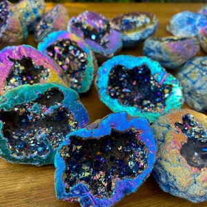 May include: A collection of iridescent, rainbow-colored agate crystal geodes. The geodes are various sizes and shapes, with a dark, black interior and a shiny, iridescent exterior.