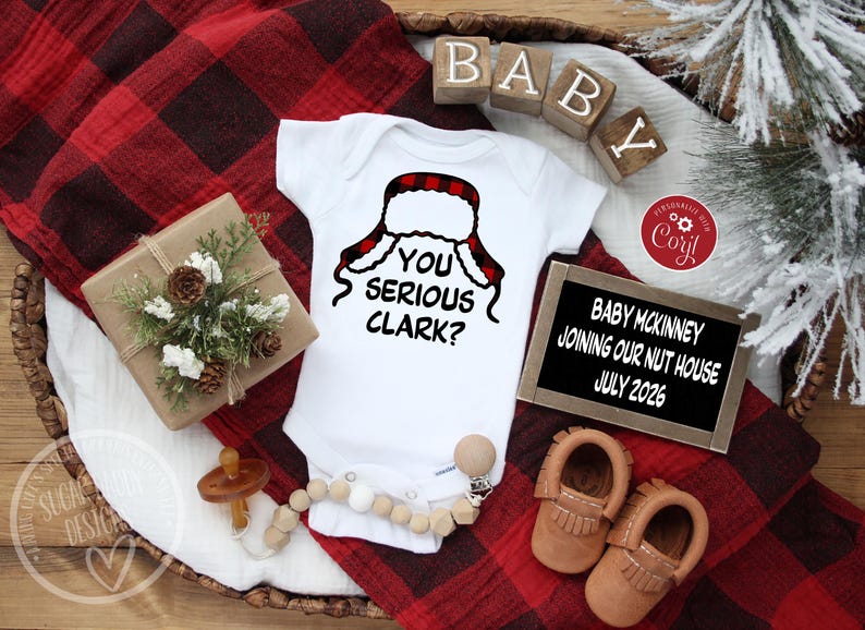 May include: A white baby onesie with the phrase "YOU SERIOUS CLARK?" and a red and black plaid hat design. The image includes baby shoes, a pacifier, and a sign announcing a July 2026 arrival.