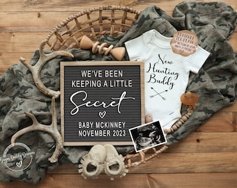 May include: A woodland-themed baby announcement with a letter board that reads "We've been keeping a little secret, Baby McKinney, November 2023". A white onesie with the text "New Hunting Buddy" and a pair of brown baby booties are also included.